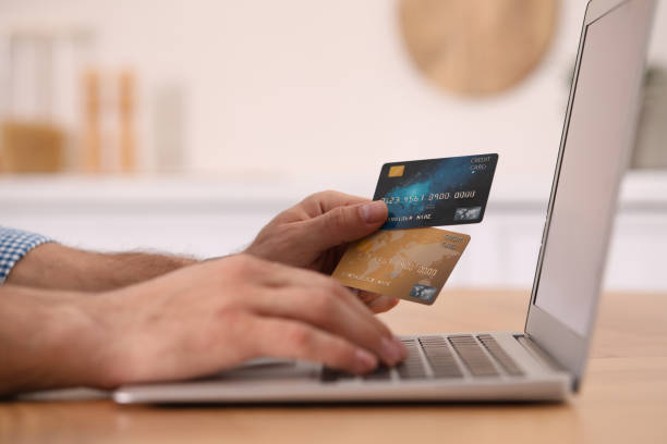 istock Man using laptop and credit cards for online payment at table in kitchen, closeup 1316598807