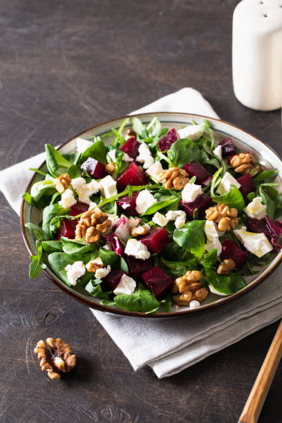 istock Beet or beetroot salad with fresh arugula, soft cheese and walnuts on plate, dressing and spices on dark wooden background, copy space, top view 1316599979