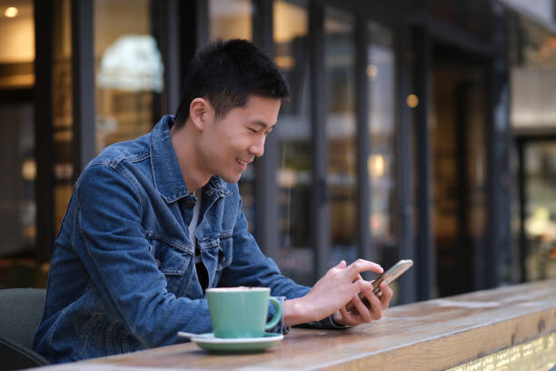 istock Asian young man at outdoor cafe, using mobile phone and smiling 1316601441