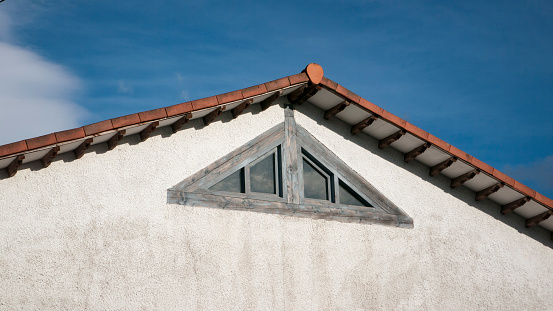 Triangular window in rural house with white wall and gabled roofs