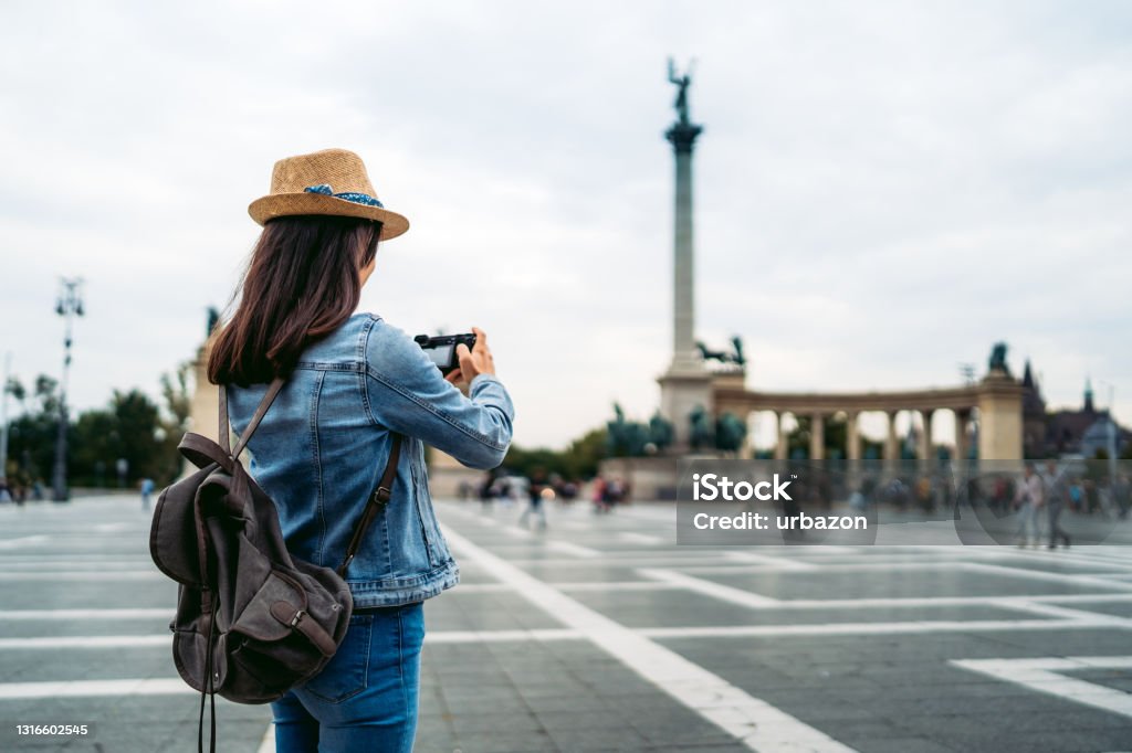 Young female tourist taking photographing Heroes Square Young caucasian female tourist taking photos on town square in Budapest. Heroes' Square/Hősök tere. Town Square Stock Photo