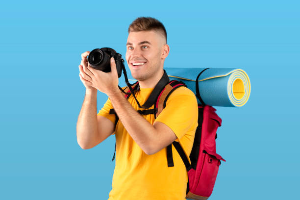 istock Postive young guy with backpack taking picture on professional DSLR camera over blue studio background 1316602799