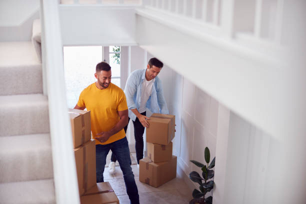 Excited Male Couple Carrying Boxes Through Front Door Of New Home On Moving Day Excited Male Couple Carrying Boxes Through Front Door Of New Home On Moving Day unpacking photos stock pictures, royalty-free photos & images