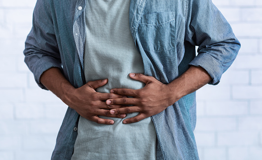 Unrecognizable Black Guy Touching Aching Abdomen Having Painful Stomachache Standing Over Gray Studio Background. African Man Suffering From Stomach Inflammation. Gastritis And Abdomen Pain. Cropped