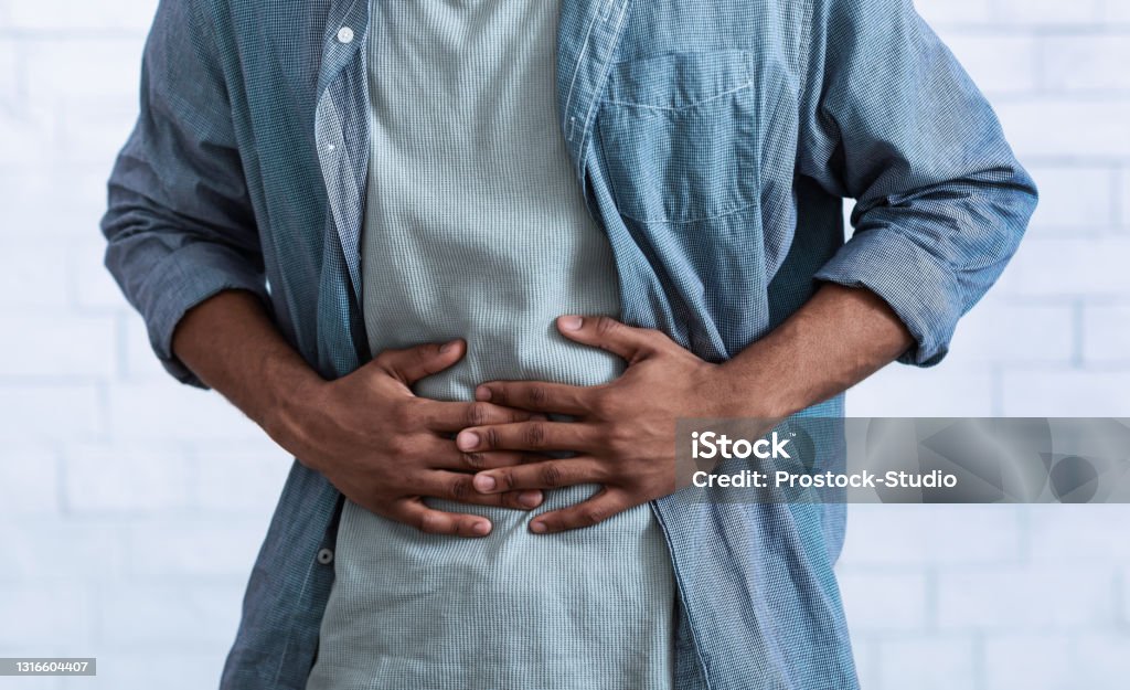 Black Guy Touching Aching Abdomen Having Stomachache, Gray Background, Cropped Unrecognizable Black Guy Touching Aching Abdomen Having Painful Stomachache Standing Over Gray Studio Background. African Man Suffering From Stomach Inflammation. Gastritis And Abdomen Pain. Cropped Stomachache Stock Photo