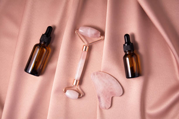 istock Quartz roller, gua sha and serum bottles on shiny pink fabric. 1316606930