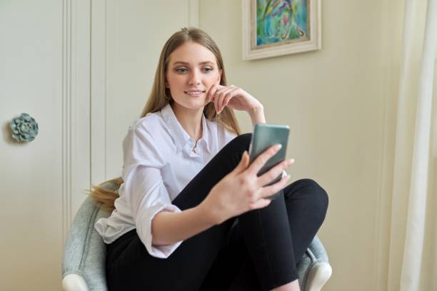 istock Young blonde sitting at home in chair, using video communication on smartphone 1316610904