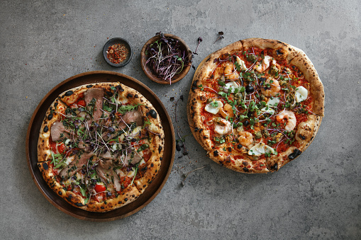 Italian seafood pizza with shrimps, squids, scallops, mussels and capers. Roast beef pizza. Flat lay top-down composition on concrete background.