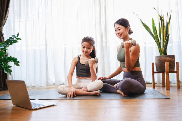 istock Mom and Little Girl doing dumbbell exercises by using online learning with a laptop computer on a yoga mat in the living room at home. New normal concept. Healthy lifestyle. Relaxing at home 1316616678