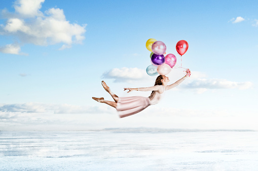 Happy ballerina is flying with her colorful balloons on a cloudy sky