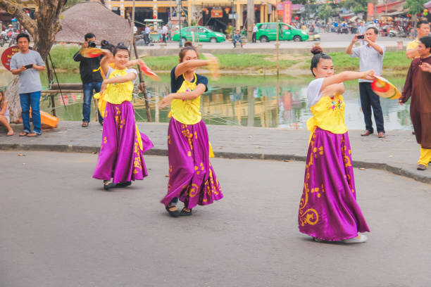 Young local Vietnamese women in colourful traditional dress and costume perform a ceremonial dance on the streets of Hoi An.