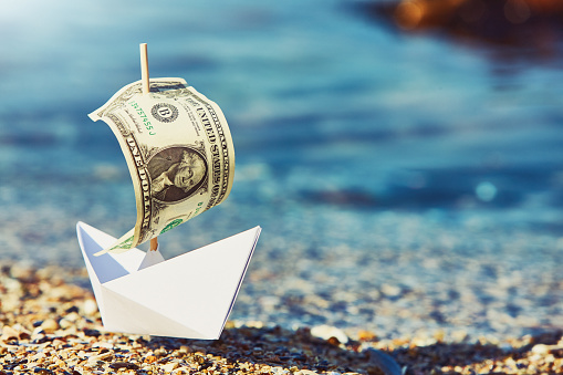 Plenty of financial concepts in this image of a paper boat with a one-dollar banknote as a sail, with copy space in the water.