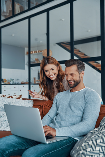Cheerful young couple using laptop and smiling while shopping online at home