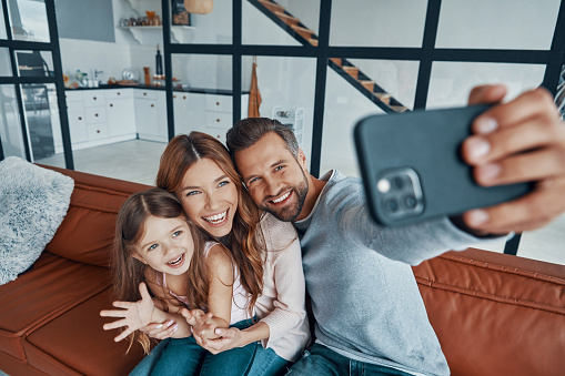 Happy young family smiling and using smart phone to take a selfie while spending time at home