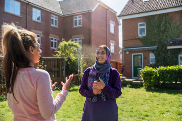 Catching Up With Friends Two female friends standing in a back garden owned by one of them, talking face to face with one another. One woman is wearing a headscarf. middlesbrough stock pictures, royalty-free photos & images