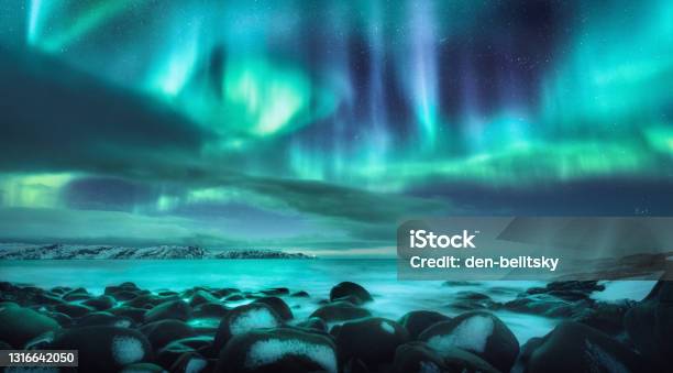 Northern Lights Aurora Borealis Over Ocean In Teriberka Russia Starry Sky With Polar Lights And Clouds Night Winter Landscape With Bright Aurora Stars Sea Snowy Stones In Blurred Water Travel Stock Photo - Download Image Now