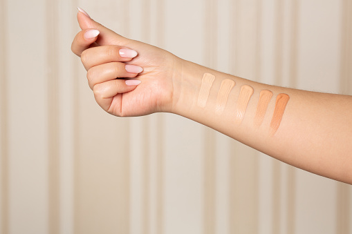 Woman applying shades from light to dark of a liquid makeup foundation on hand. Closeup shot