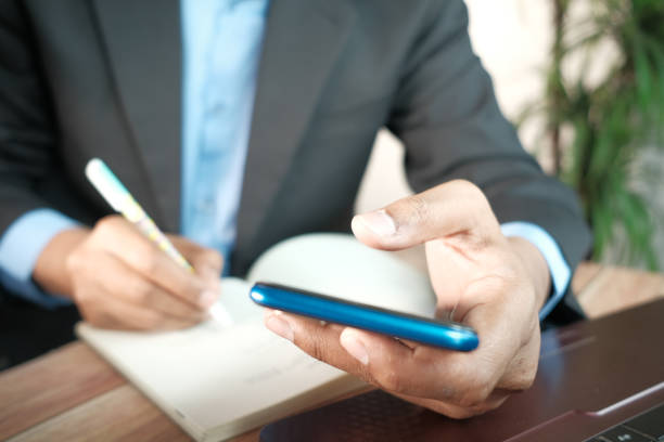 istock Close up of young man hand using smart phone and writing on notepad 1316647143