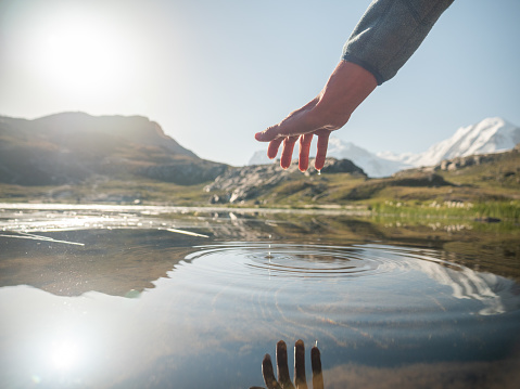 Detail of hand touching water in mountain lake below glacier