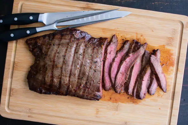 Sliced medium-rare flank steak on a bamboo carving board