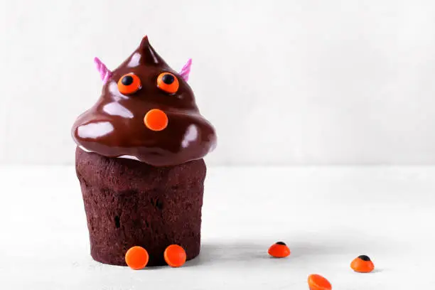 Chocolate cupcake with cute face and sugar horns on the white table. Halloween dessert for kids. Creative food