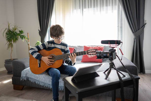 jeune garçon adolescent blogueur vidéo est d’enseigner à jouer de la guitare en ligne à la maison sur la caméra - youtube home video camera internet ipad photos et images de collection