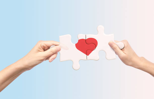 Hands holding white jigsaw with red heart shape inside stock photo