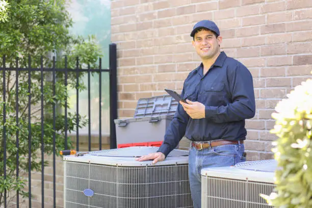 Latin descent, blue collar air conditioner repairman working at residential home.  He prepares to begin work by gathering appropriate tools and referring to digital tablet.