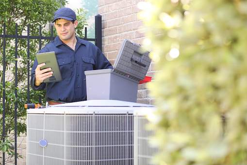 technician working on air conditioning or heat pump outdoor unit. HVAC service, maintenance and repair