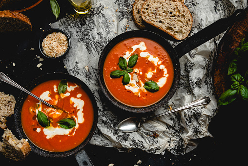 Flat lay of two pots of tomato soup with cream and basil