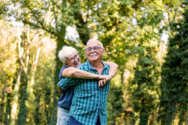 Portrait of beautiful senior couple hugging and posing in the spring park Portrait of a happy older man carrying his beautiful wife on his back in the woods. The older couple is enjoying their vacation. older woman purse stock pictures, royalty-free photos & images