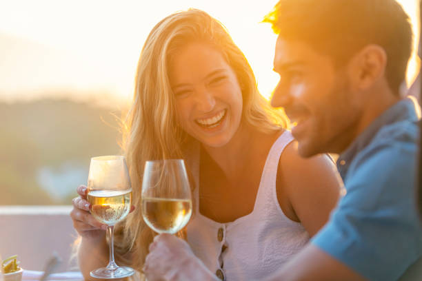 Romantic couple flirting and drinking wine outdoors. Romantic couple flirting and drinking wine outdoors. Some food can be seen on the dinner table. Time is sunset. Both are happy and smiling and laughing couple drinking stock pictures, royalty-free photos & images