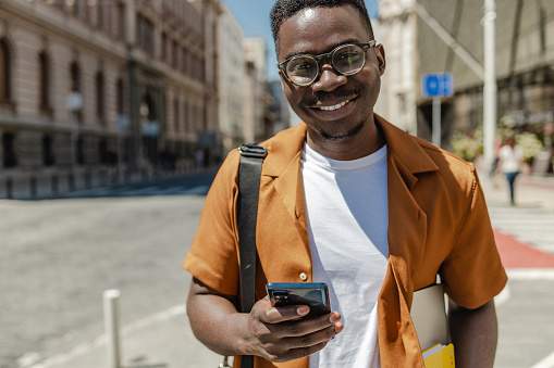 Portrait of an African-American man on the street, he is carrying a laptop and using a mobile phone