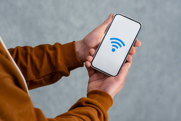 istock Man hand holding silver smartphone isolated on light background. Phone mockup with white screen and wi-fi icon. 1316682595