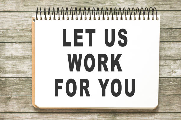 istock Text Let us work for you on notebook page on wooden table in office workspace. Business concept 1316683528