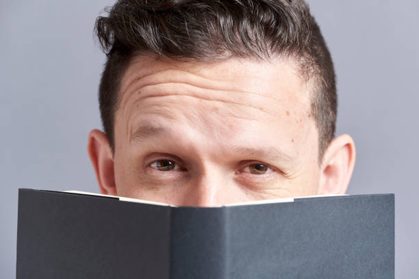 istock Man looking at the camera raising an eyebrow, peeking out from behind a book 1316689008