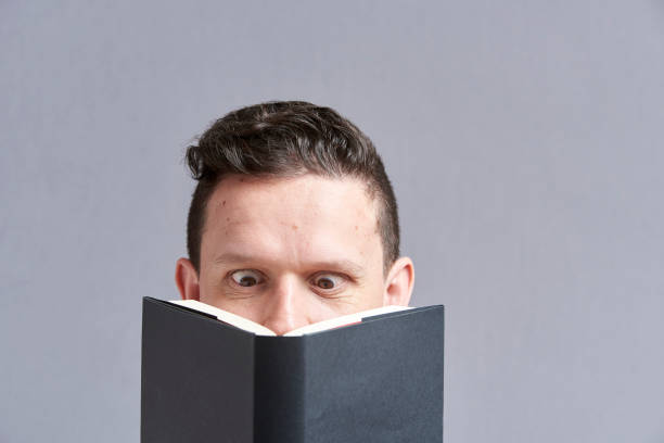 istock Young man reading a black book with squinted eyes; a comical, funny look 1316689204
