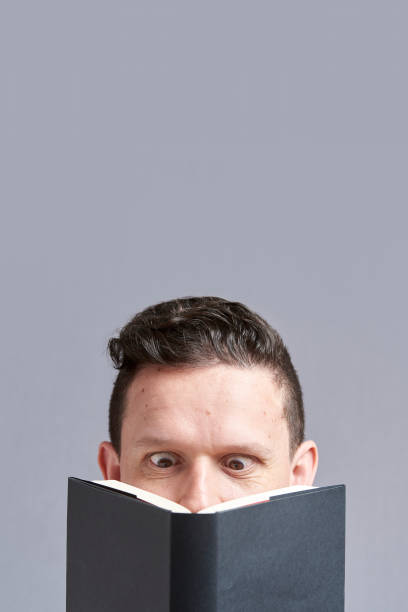 istock Young man reading a black book with squinted eyes; a comical, funny look 1316689252