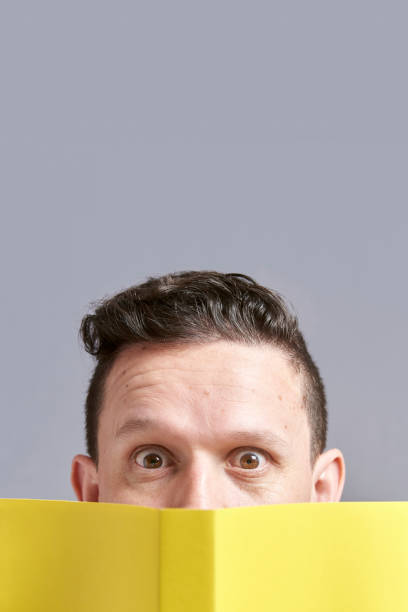 istock Young man looking at the camera, peeking out from behind an open yellow book 1316689432