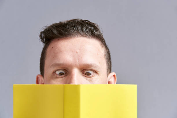 istock Young man reading a yellow book with squinted eyes; a comical, funny look 1316689456