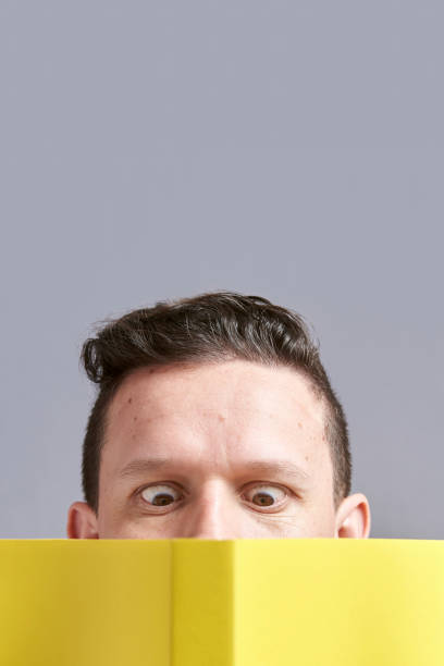 istock Young man reading a yellow book with squinted eyes; a comical, funny look 1316690003