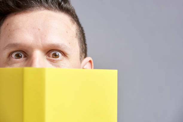 istock Young man looking at the camera, peeking out from behind an open yellow book 1316690310