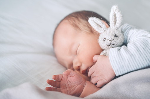 Newborn baby sleep at first days of life. Portrait of new born child boy one week old sleeping peacefully with a cute soft toy in crib in cloth background.