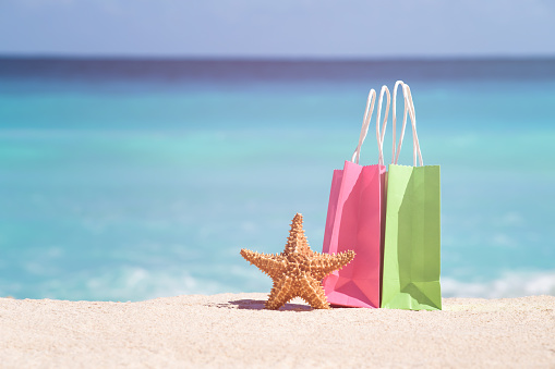 Shopping bags and starfish on sand against turquoise caribbean sea water. Tropical celebration on beach