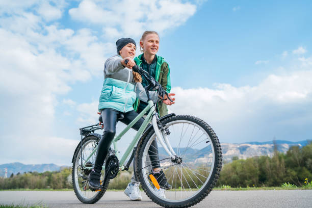 istock Brother helping to sister, supporting her and teaching doing first steps in riding. Kids on a bicycle path with wide blue cloudy sky background. Happy childhood concept image. 1316693816
