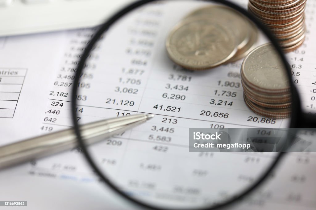 View at financial details in table thru magnifying glass View at financial details in table thru magnifying glass close-up Accountancy Stock Photo