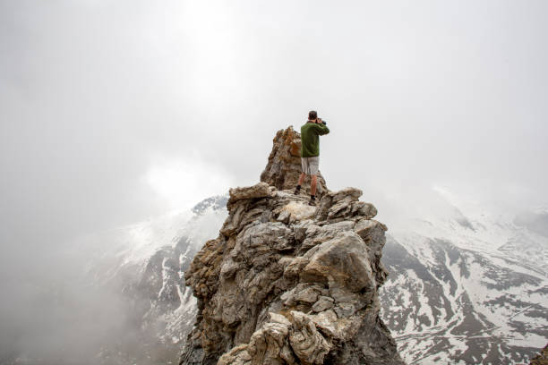 하이커는 바위 절정에 휴식을 취하고 카메라에 사진을 찍습니다. - men on top of climbing mountain 뉴스 사진 이미지