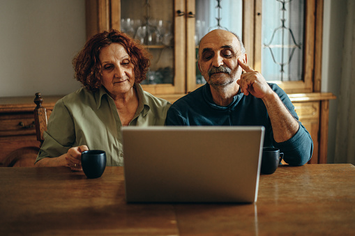 Senior couple using a laptop for a video call with their family while relaxing at home and drinking coffee