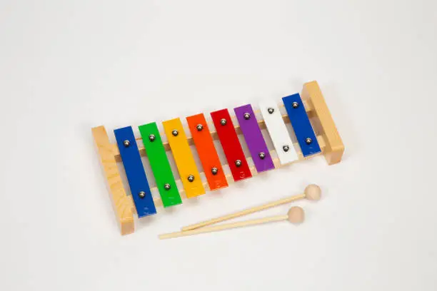 Child’s xylophone instruments made of wood and metal with wooden mallets laying by the side. Keys are brightly colored in blue, yellow, orange, red, purple, and white.