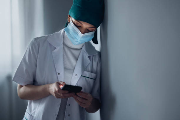kvinnlig kirurg skriver meddelande på smartphoneâ i korridoren på sjukhuset - nurse on phone serious bildbanksfoton och bilder